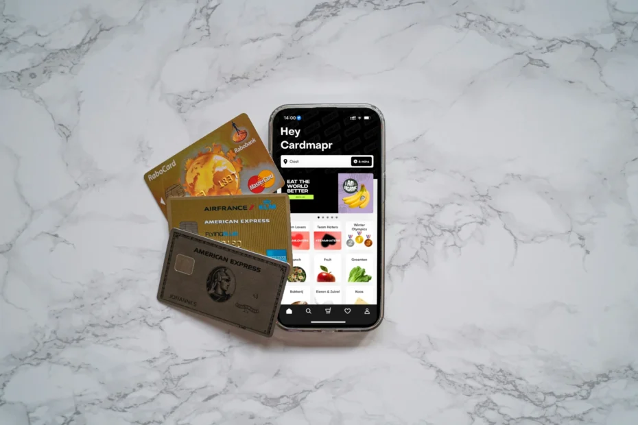 Imagen de tarjetas de crédito, incluyendo la Blue Cash Preferred de American Express, acompañada de un teléfono móvil que muestra una aplicación financiera.